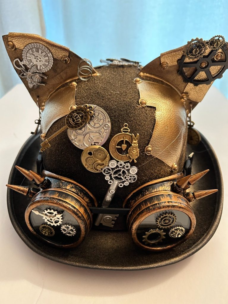 A brown bolo hat decorated in steampunk style with goggles and other steampunk themed items.