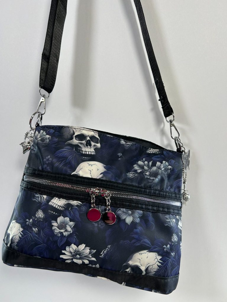 A black Goth style black purse with skulls and other objects on it.