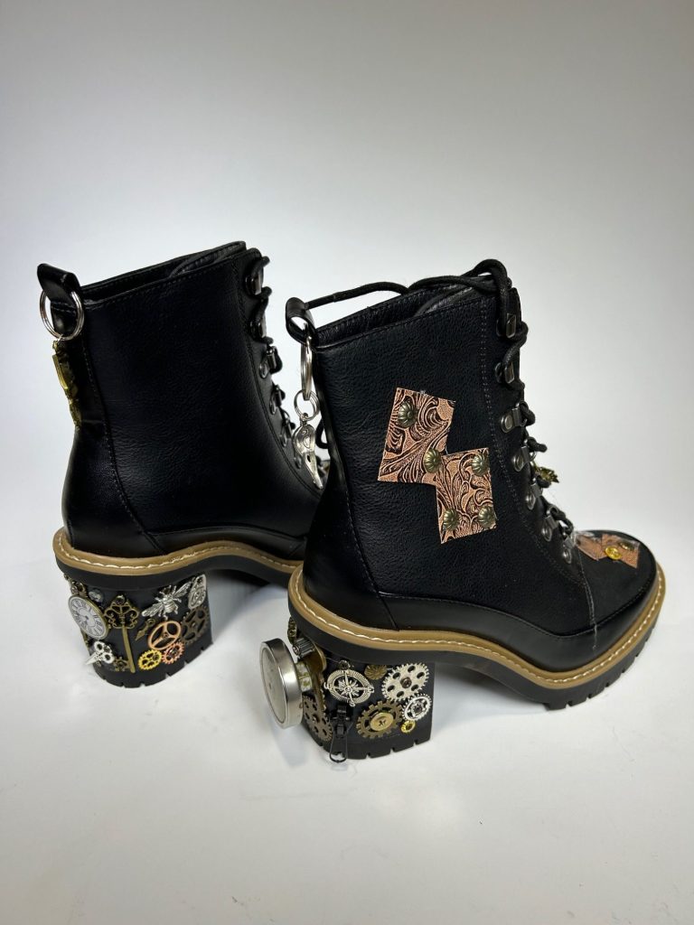 A pair of black hi top leather boots decorated with steampunk style accessories.